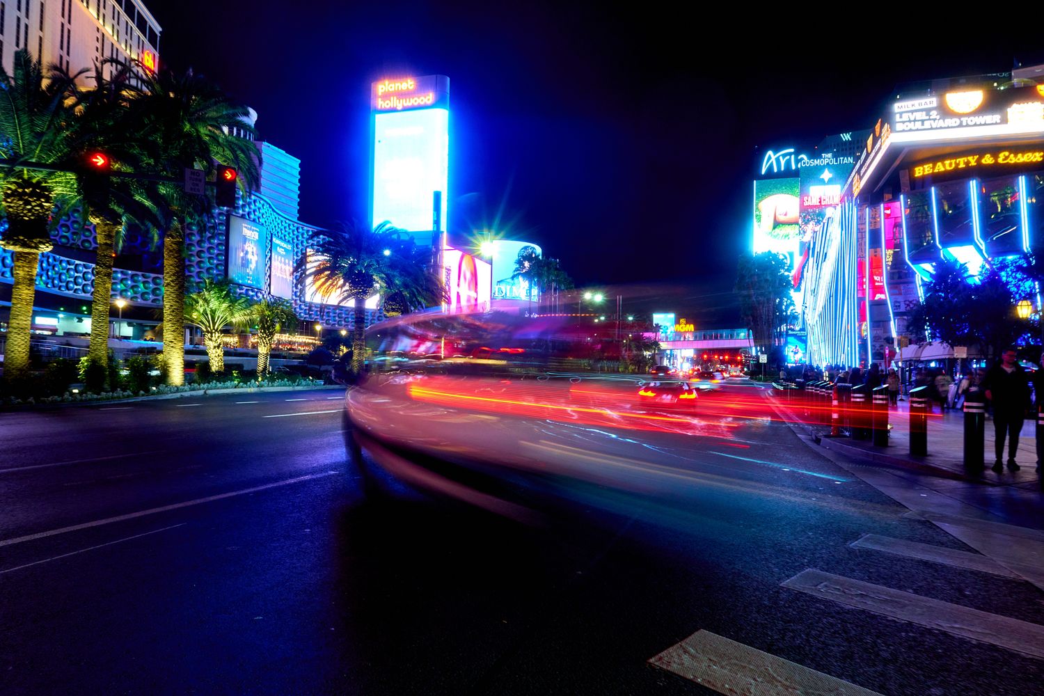 City street at night with blue neon lights and motion blur from passing vehicles.