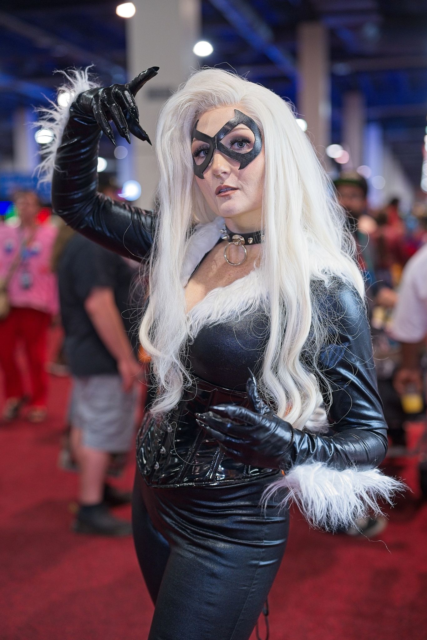Cosplayer in black leather outfit with white wig and mask posing at convention.