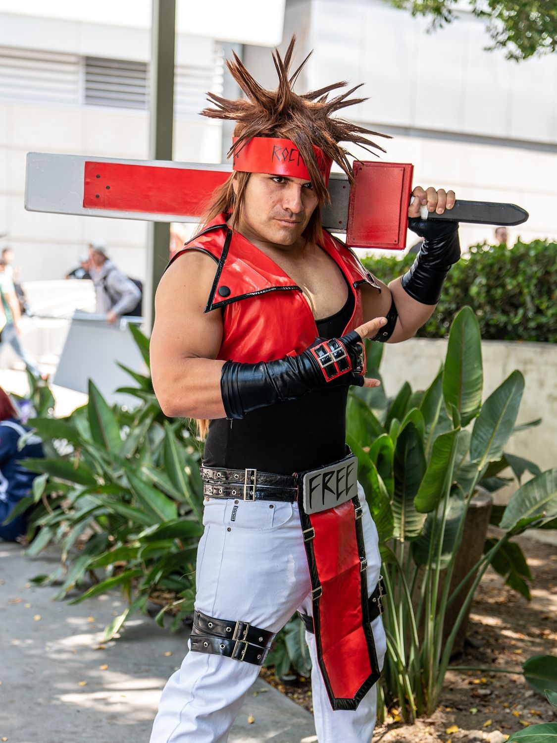 Cosplayer in red and black combat outfit with metallic accessories posing outdoors.