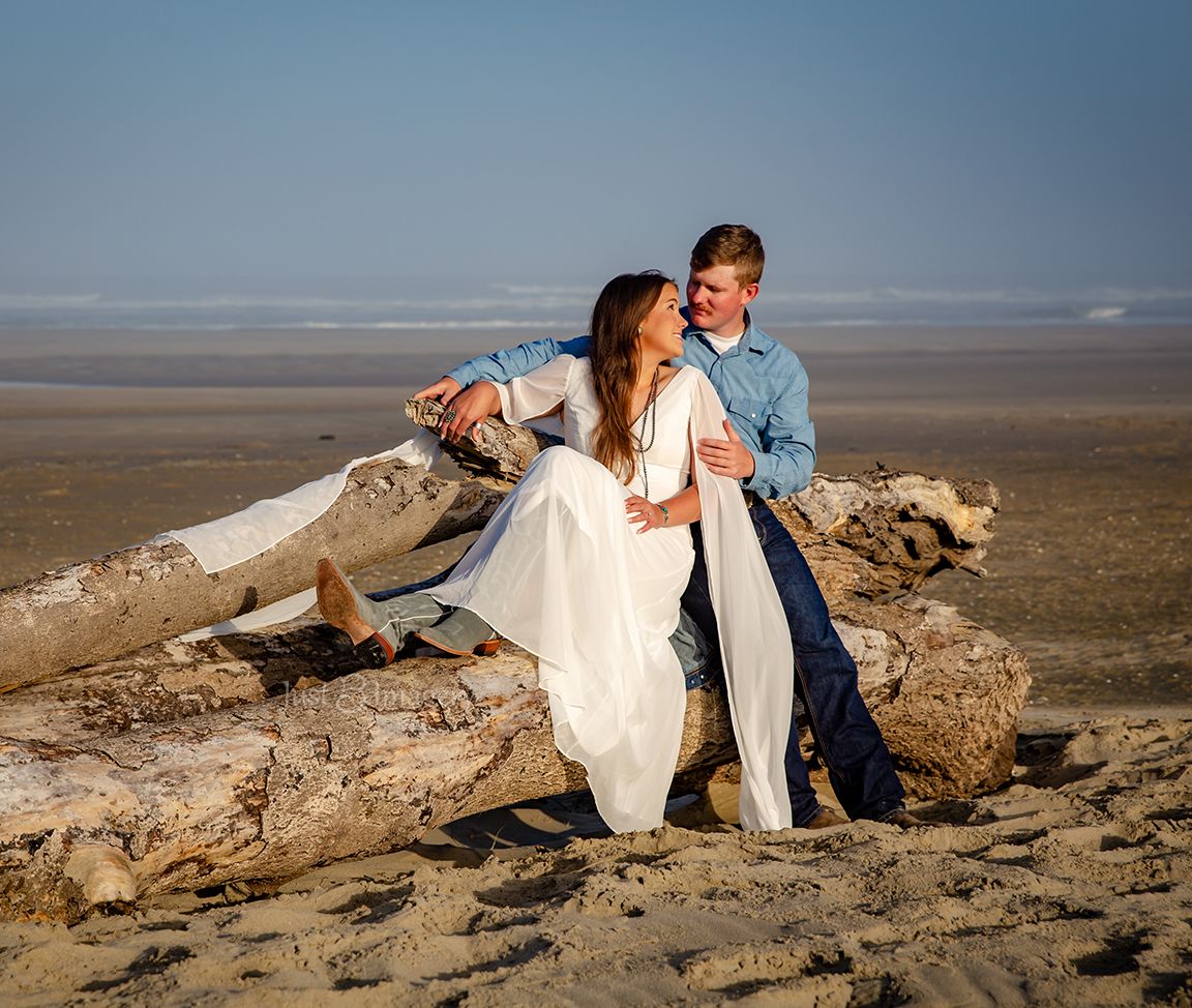 engaged couple sitting on driftwood at the beach in Oregon in the full sun