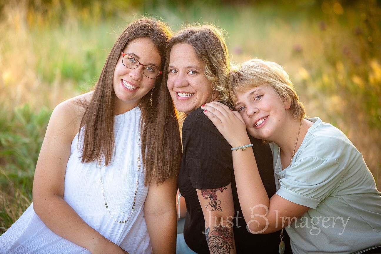 mom and teenage daughters sitting close to each other in a glowy field
