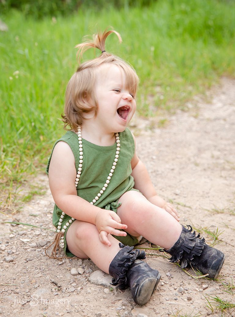 toddler sitting on a gravel path with green grass smiling and being sassy