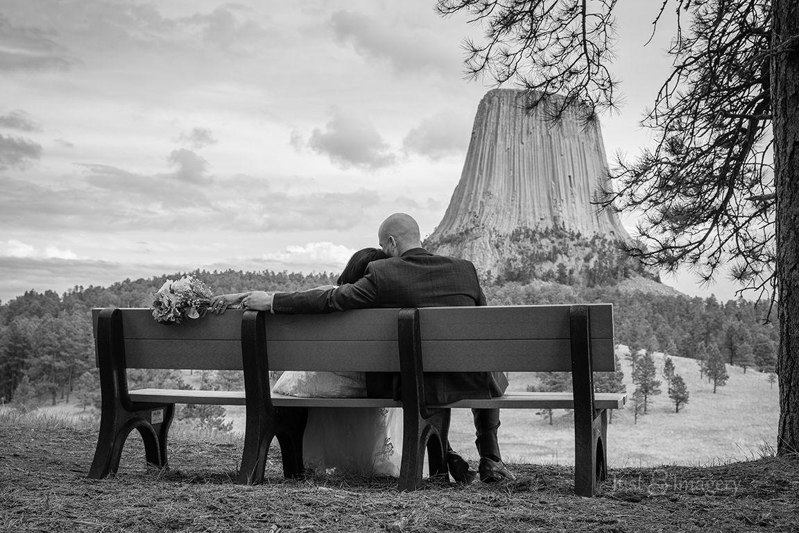bride and groom sitting on park bench after wedding enjoying view of Devils Tower, black and white