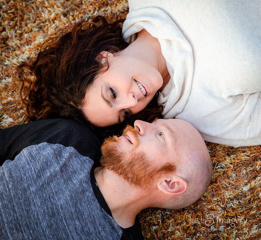 engaged couple looking at each other while laying on a blanket on the ground