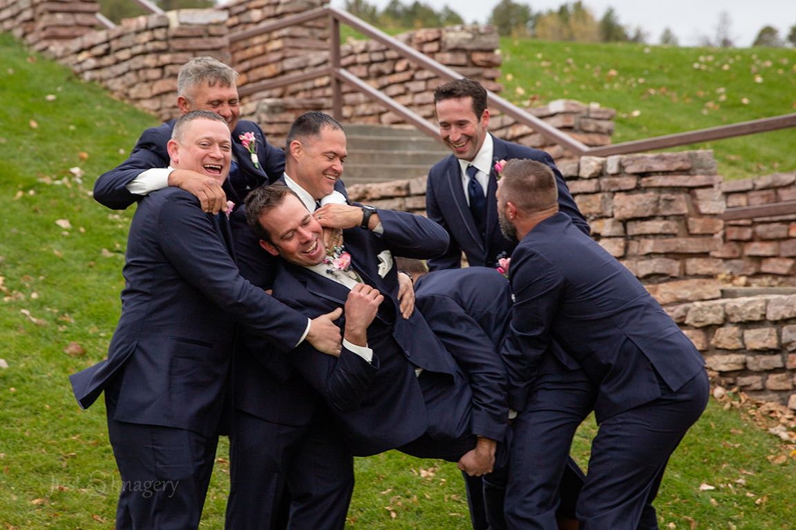 groomsmen carry of groom before the wedding in a green park