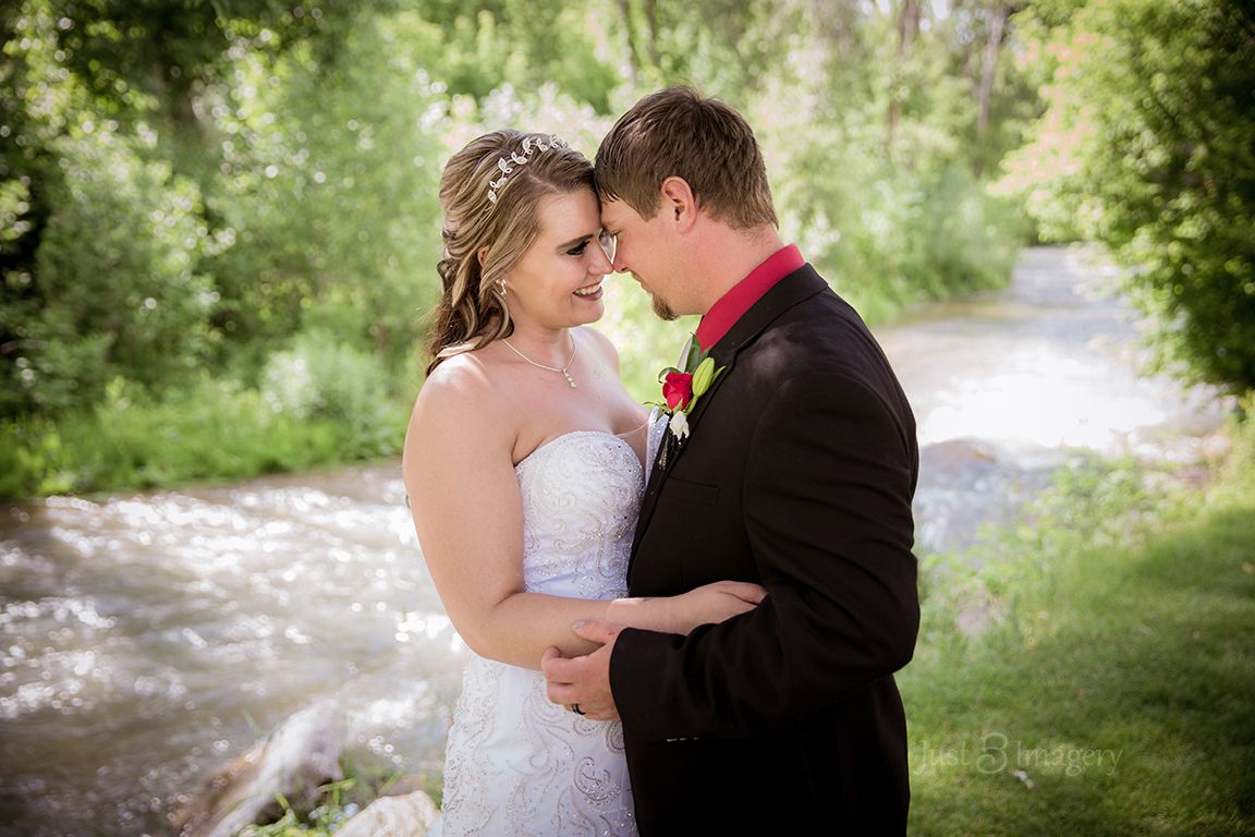 bride and groom stand next to creek and look lovingly at each other