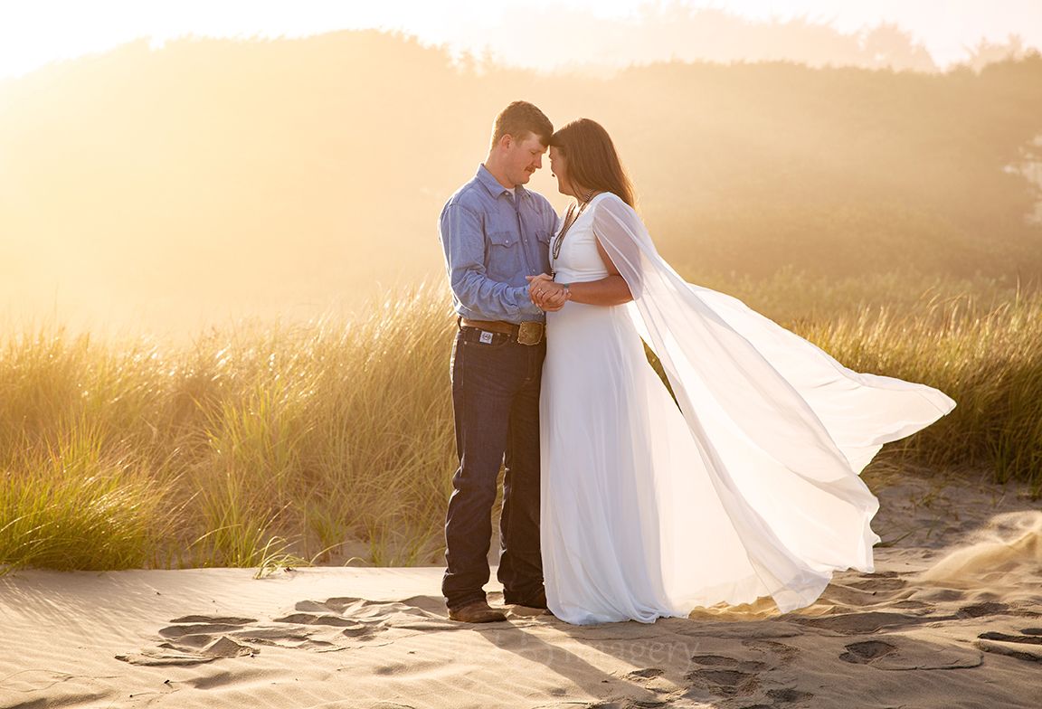 engaged couple stand in the fog on the beach looking at each other in love