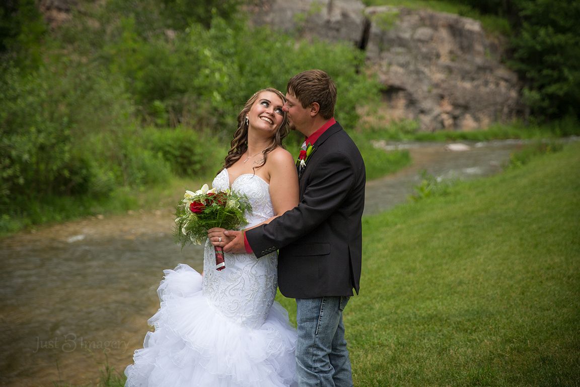 wedding couple standing along creek, green grass