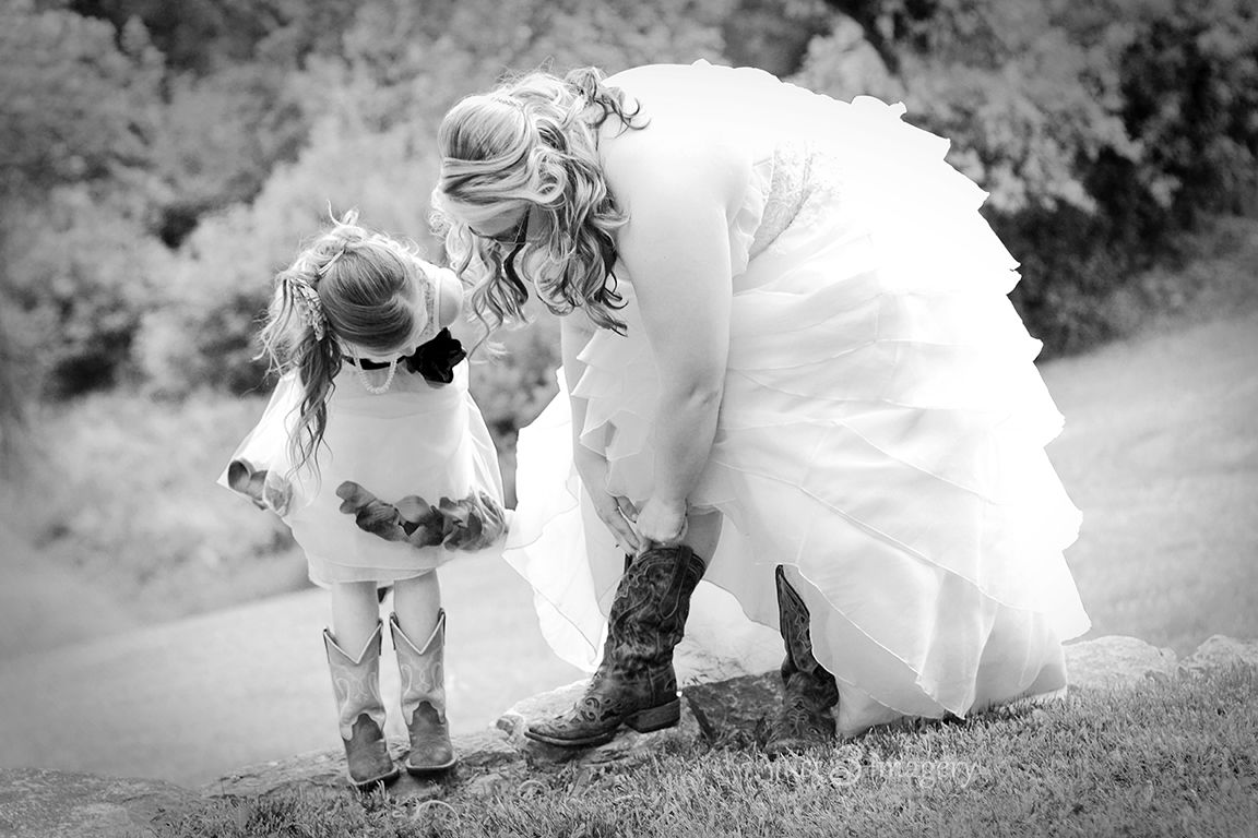 bride adjusts her boots under her wedding dress with the flower girl looking on, black and white