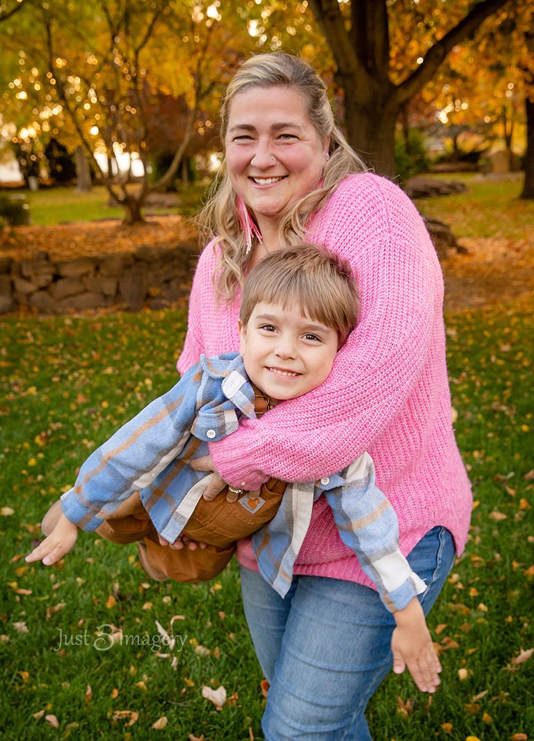 grandma flying young grandson around like an airplane in her arms, fall in the park, golden trees