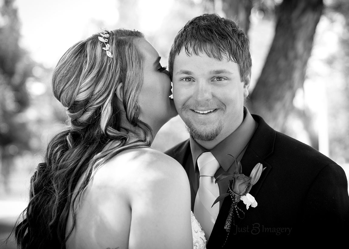 bride whispering in groom's ear while he smiles at the camera, black and white