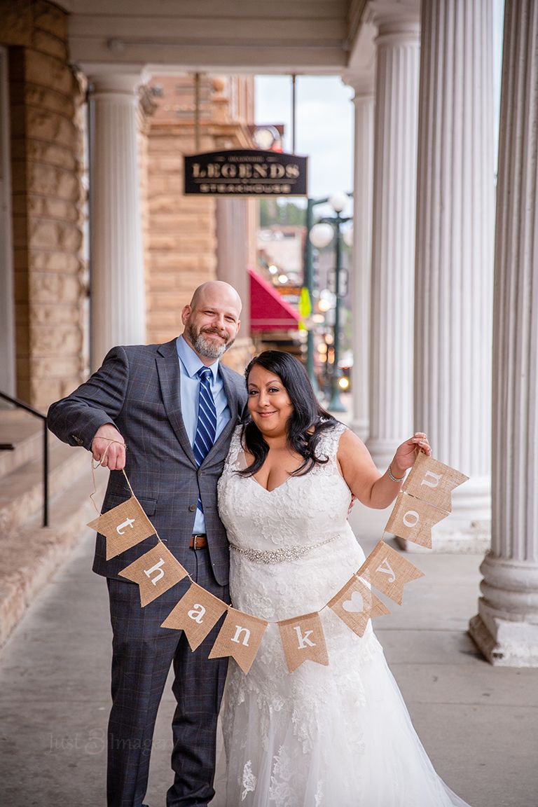 bride and groom standing under old downtown balcony holding a thank you banner