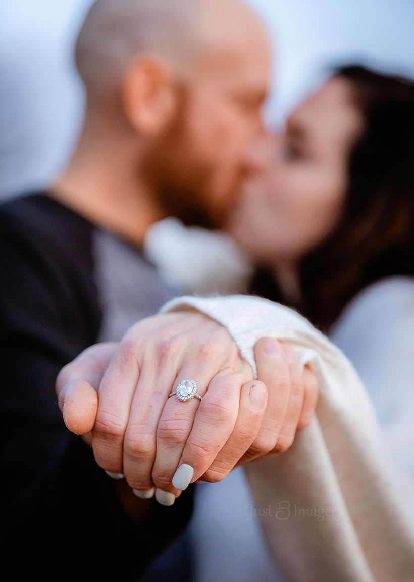 engaged couple kiss each other with engagement ring in focus