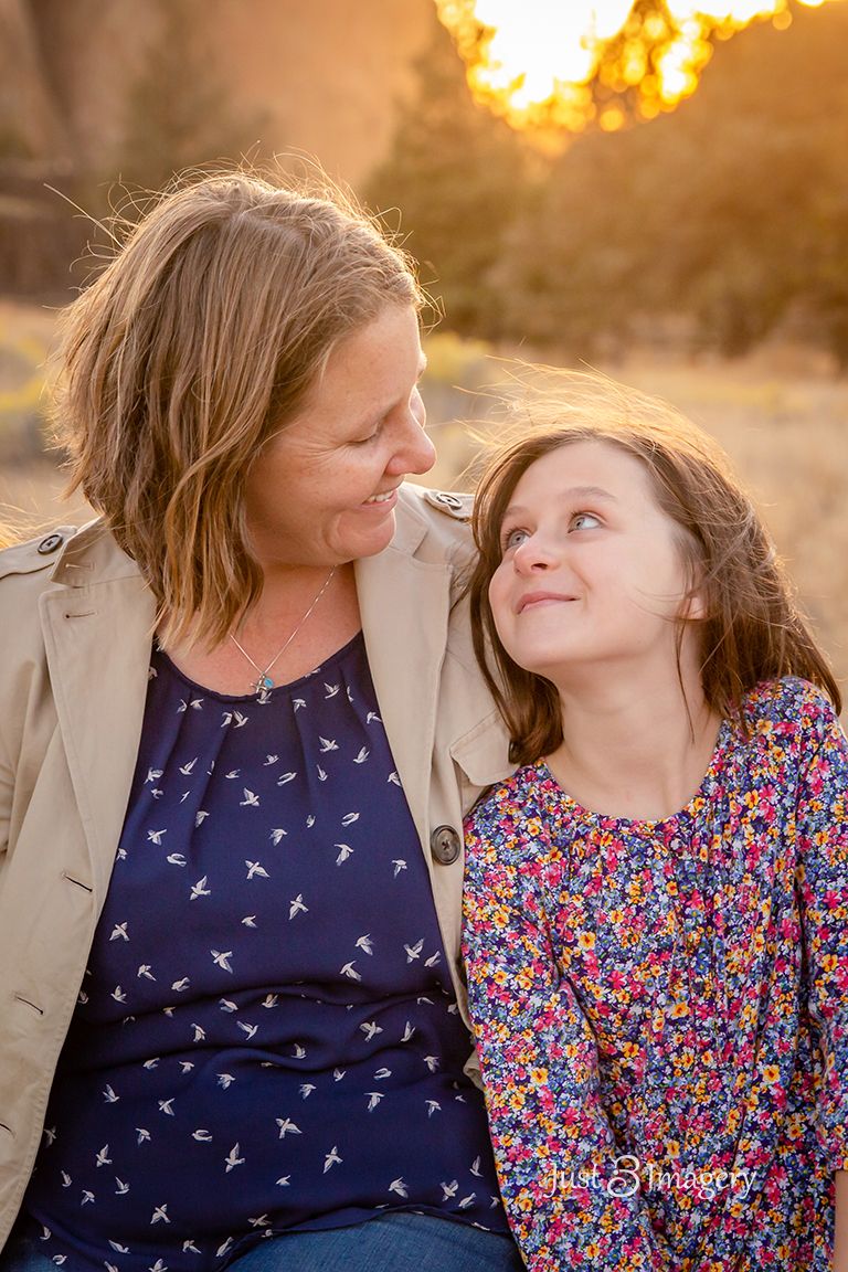 mom and daughter looking at each other smiling with a glowy sunset background at Smith Rock