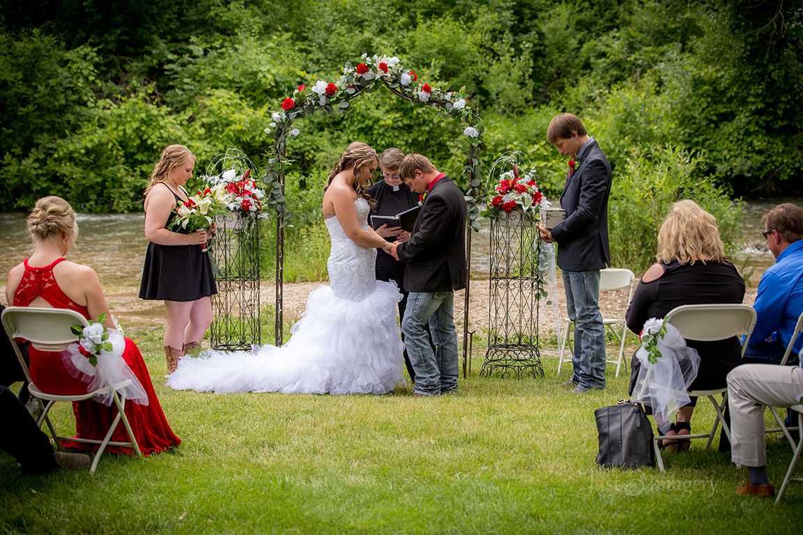 wedding ceremony along a creek with the bridal party and guests in a green park