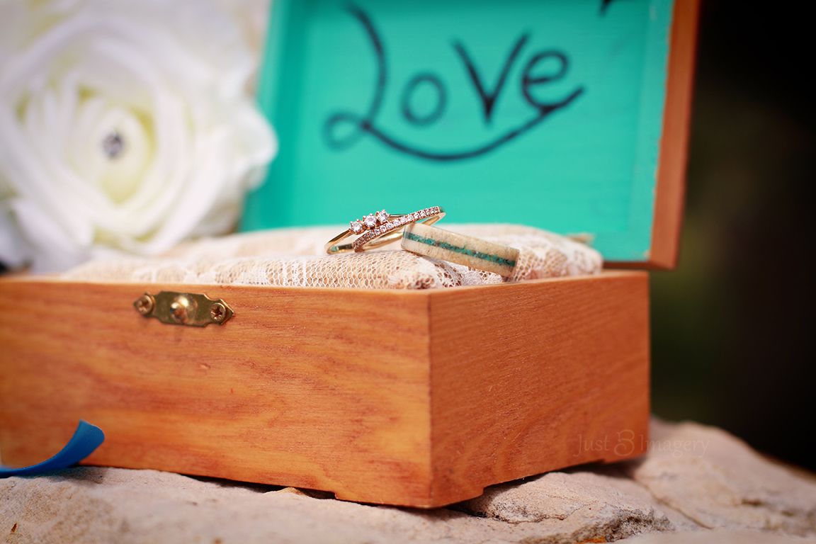 wedding rings sitting in a jewelry box with teal lid and white rose