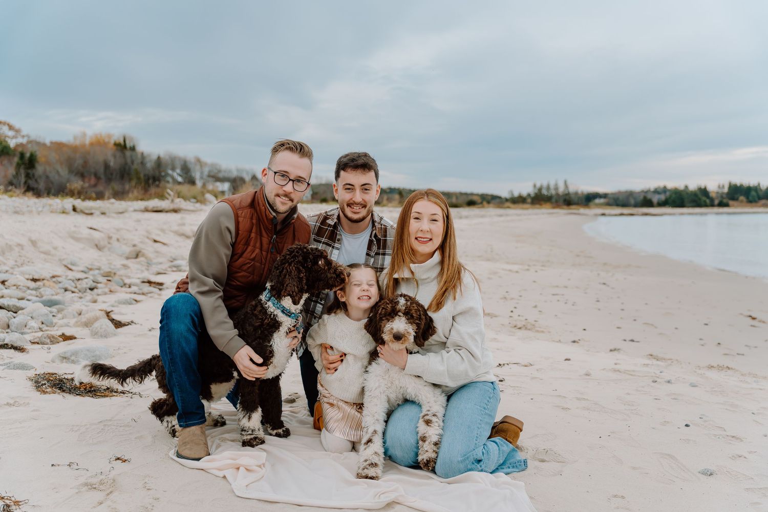 Family and their brown spaniel dog pose together on a sandy beach during a casual outdoor photo session.