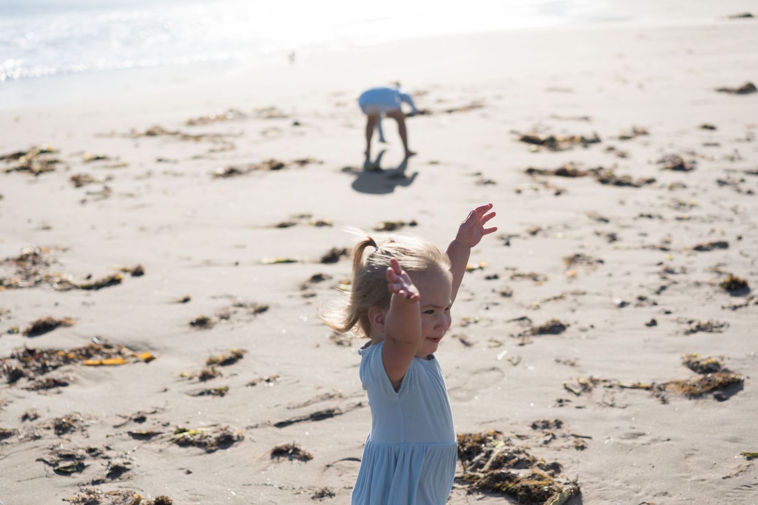 A person in a light blue dress walks along a sandy beach on a sunny summer day.
