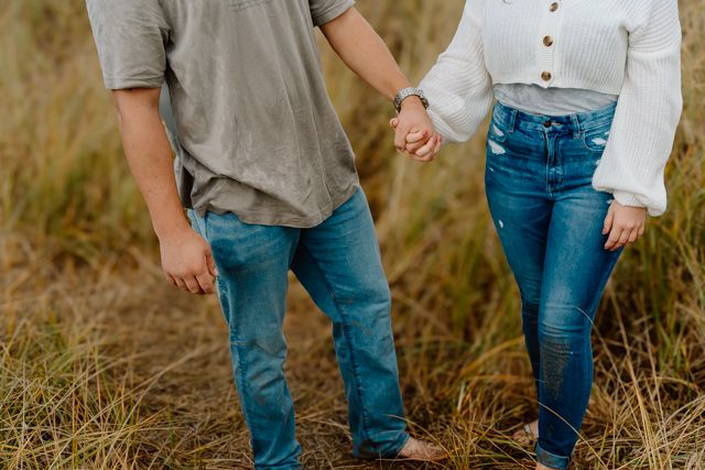 Couple walking through tall grass field during golden hour.