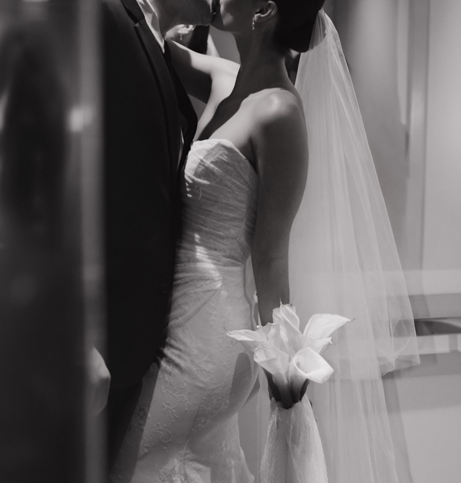 A romantic black and white wedding photo showing a couple in formal attire with a white lily bouquet.