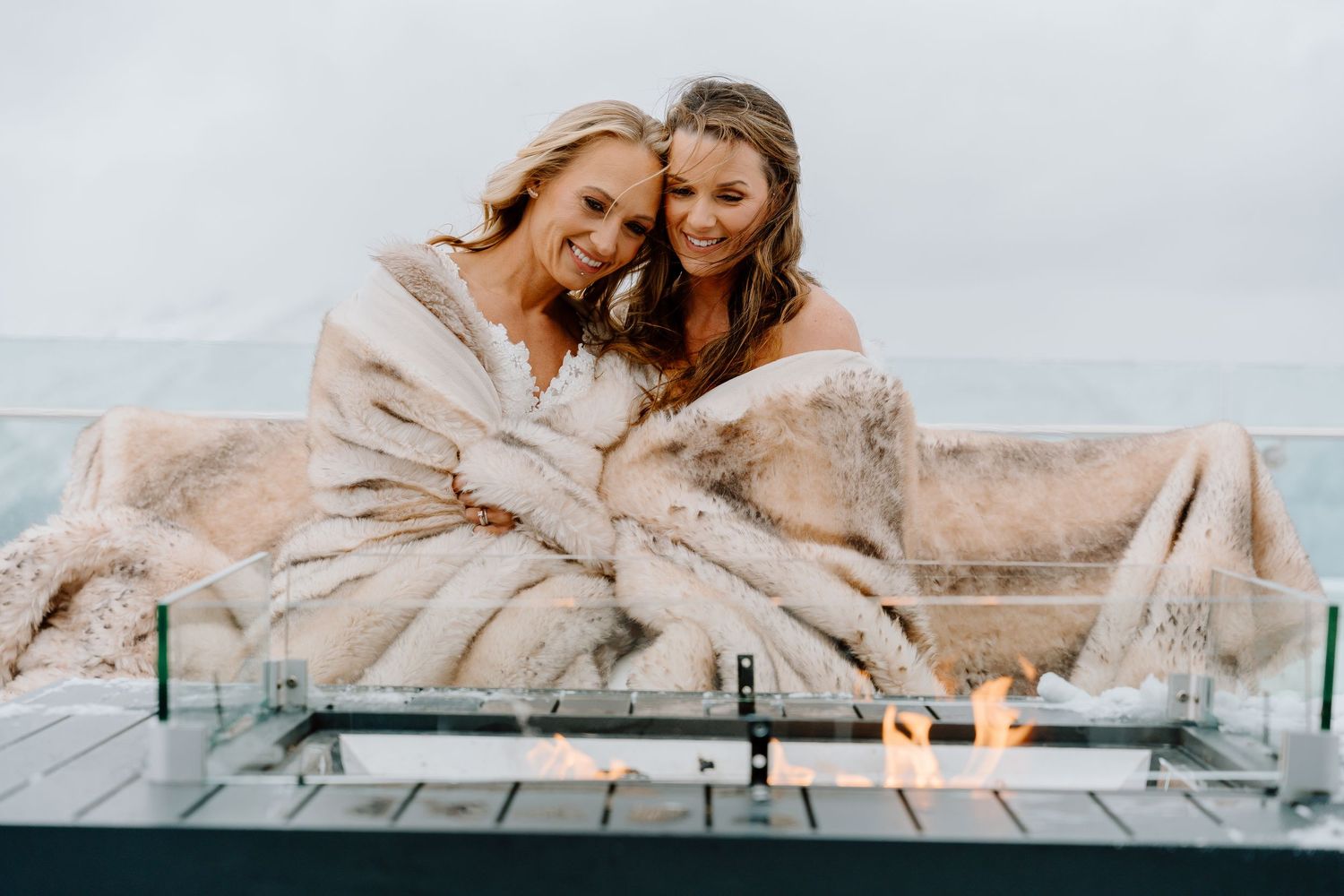 Two brides share tender moments on a snow-covered mountain deck.