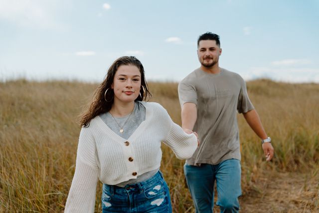 Couple walking through sunlit field wearing casual denim and neutral colors.