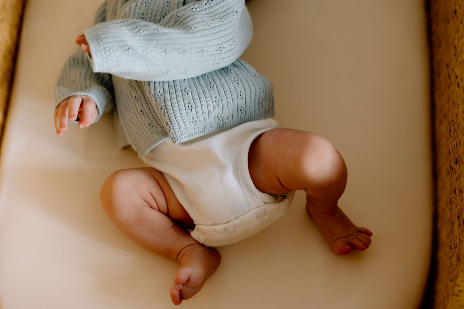 Close-up details of baby wearing soft gray clothing on neutral background.