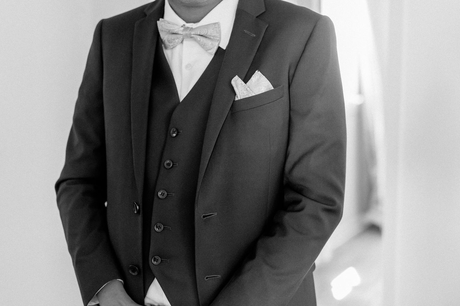 A person in a dark three-piece suit and white dress shirt poses against a light background in a formal portrait.