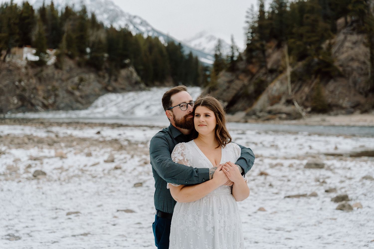 Newlyweds share tender moments along a snowy mountain lake shore.