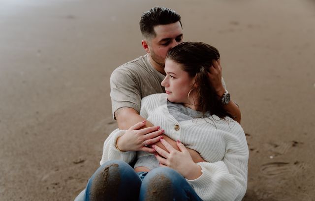 Tender embrace between couple sitting on beach sand.