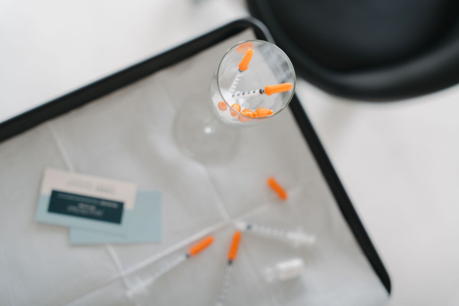 Medical syringes with orange caps arranged on a tray beside a glass container and medical packaging.