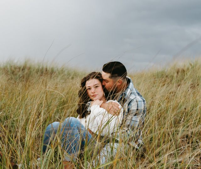 Romantic couple embracing in tall grass field during overcast day.