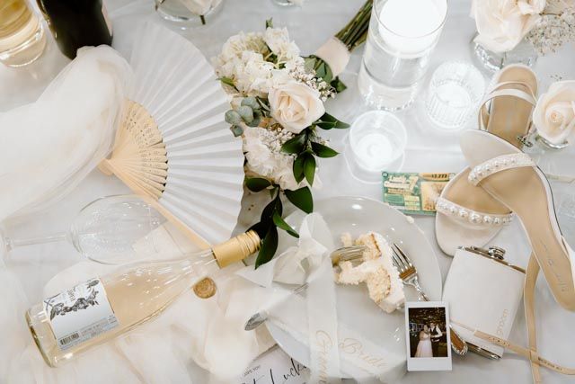 Wedding details flatlay with white paper fans, flowers and delicate decor elements.