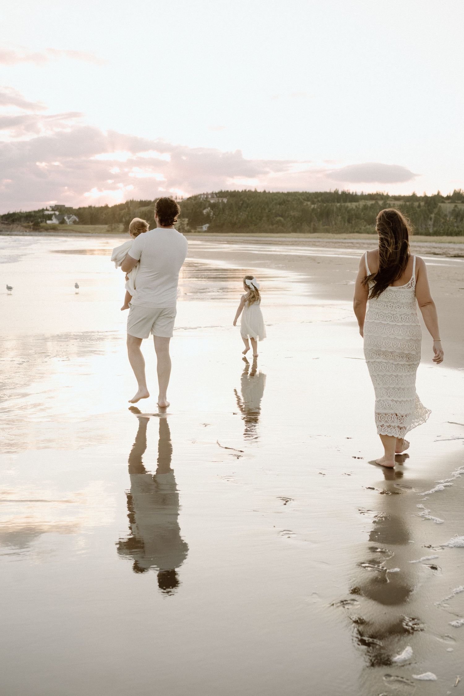 Family walking together on reflective wet sand during sunset at the beach.