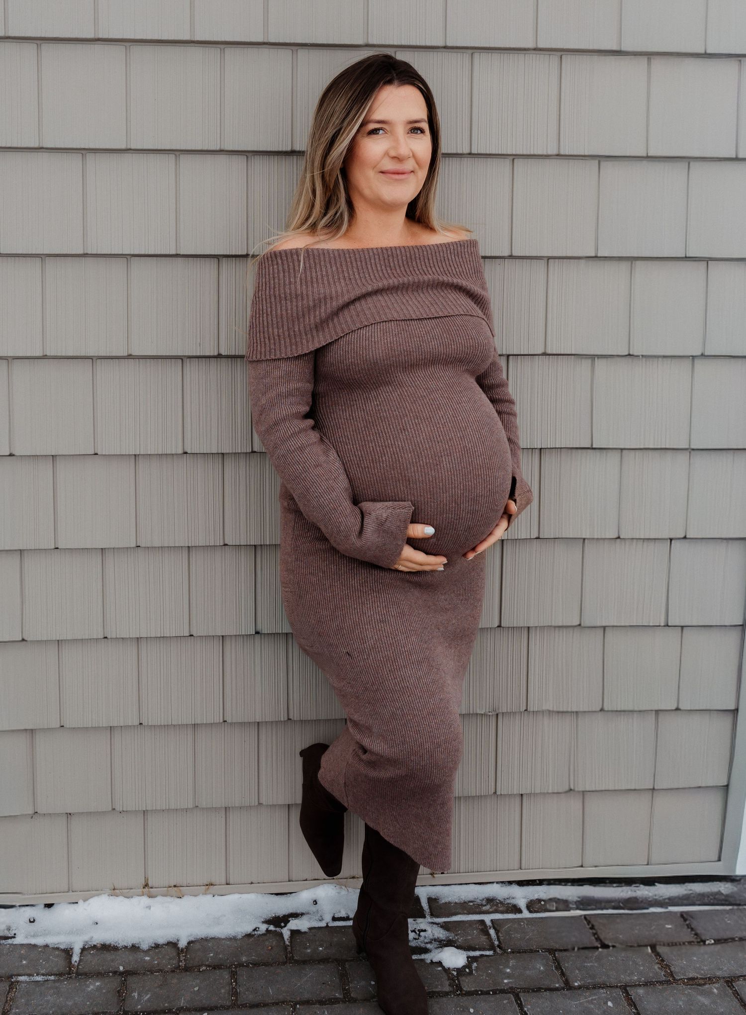 Pregnant woman in brown off-shoulder sweater poses against grey wall in maternity photoshoot sequence.