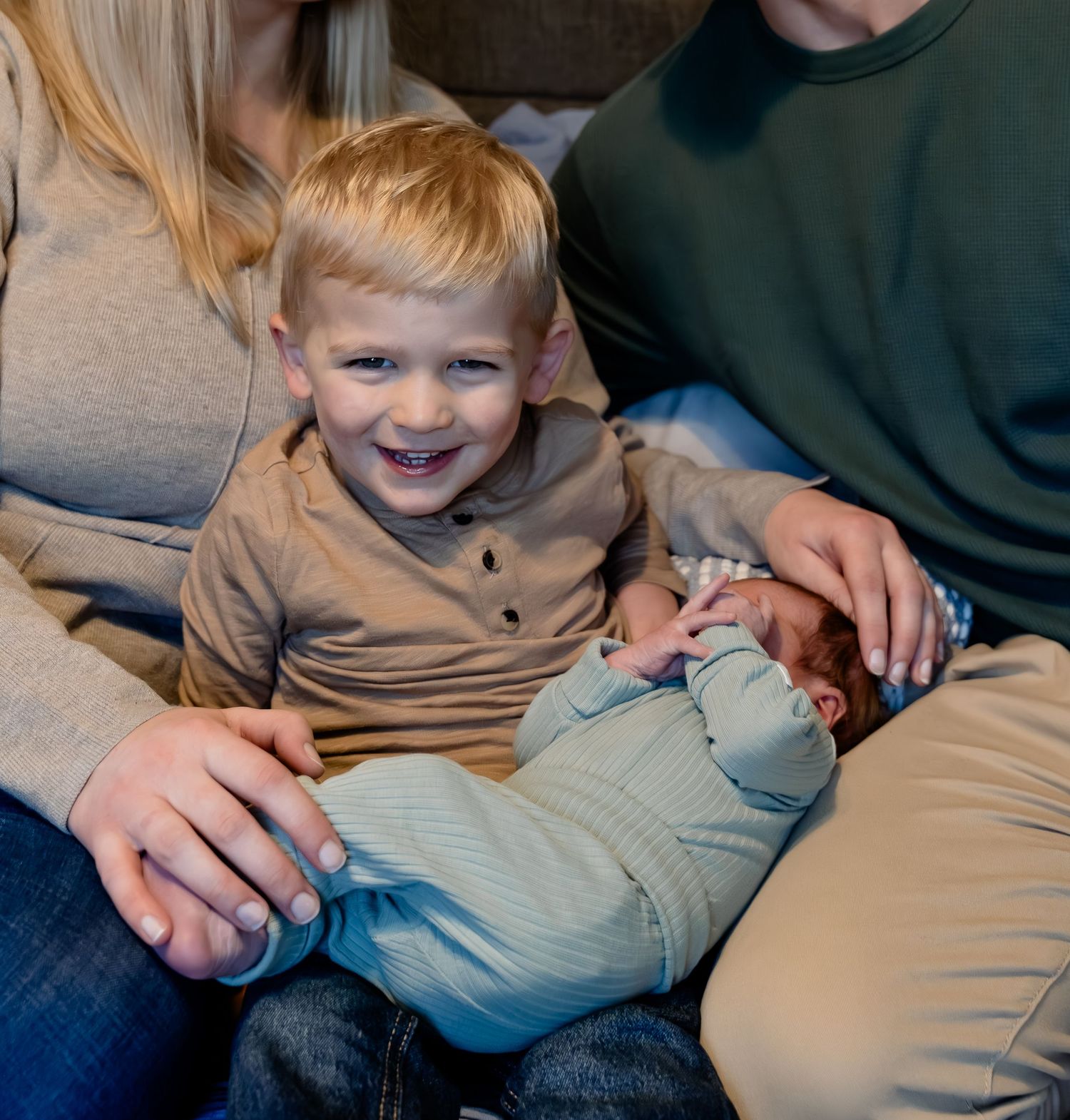A child in a gray sweater lies on a couch while being tickled, showing pure joy and laughter.