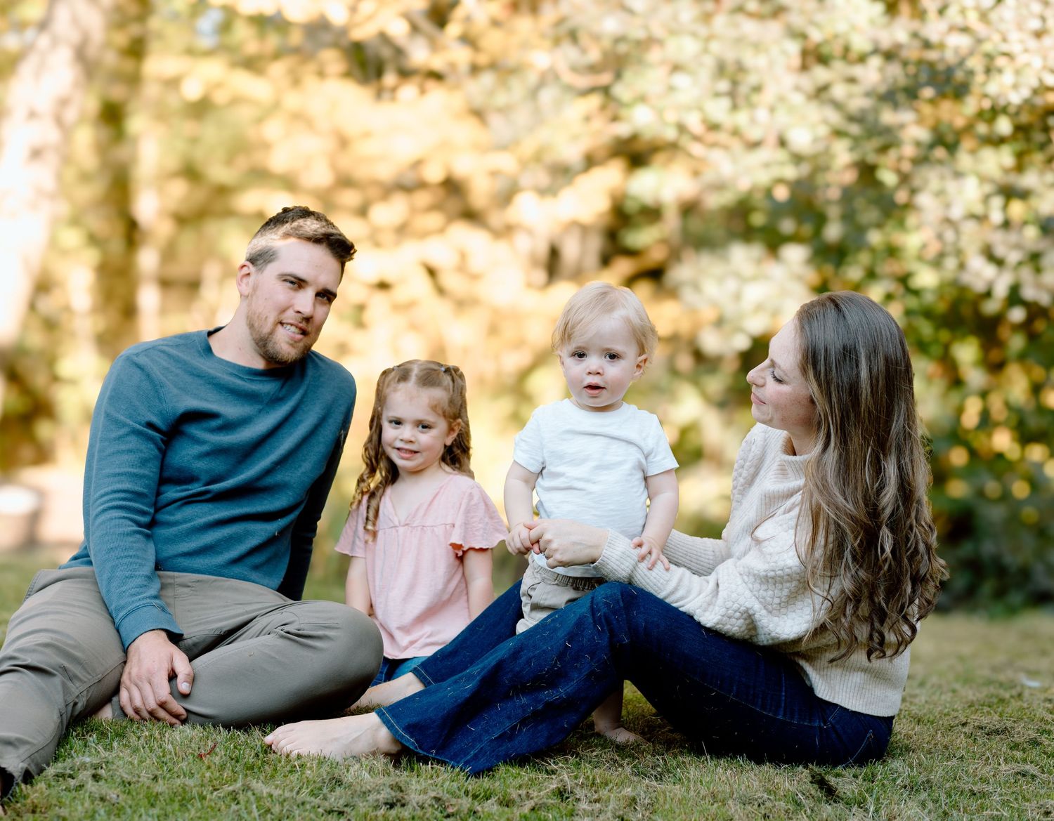 Family relaxes together on grass during golden hour photo session.