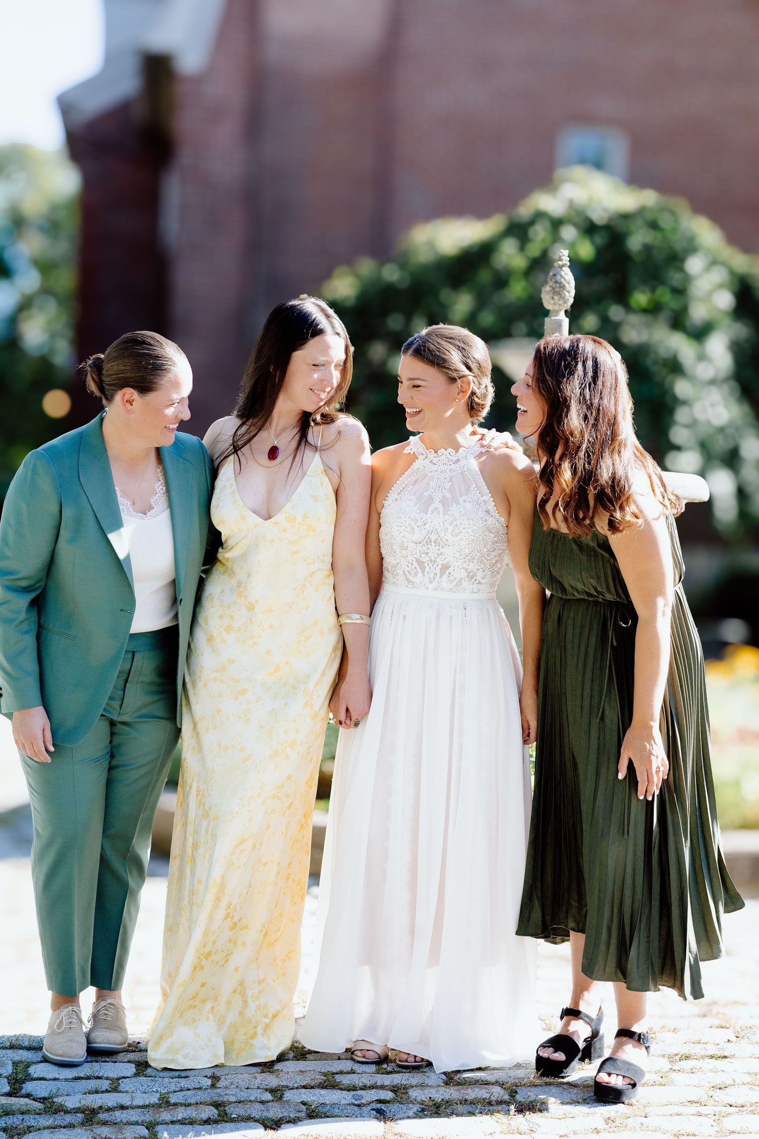Wedding party poses together wearing green dresses and yellow gowns on a sunny outdoor walkway.