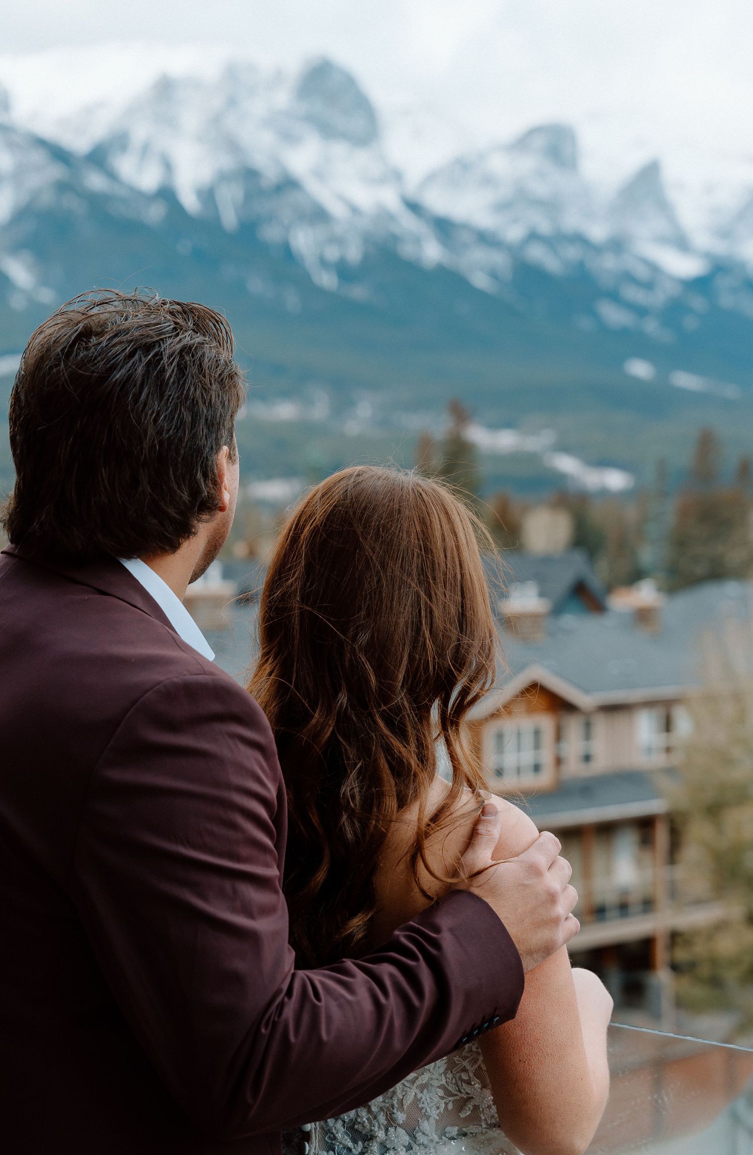 A couple embraces while admiring snowy mountain peaks and chalets in a scenic mountain landscape.