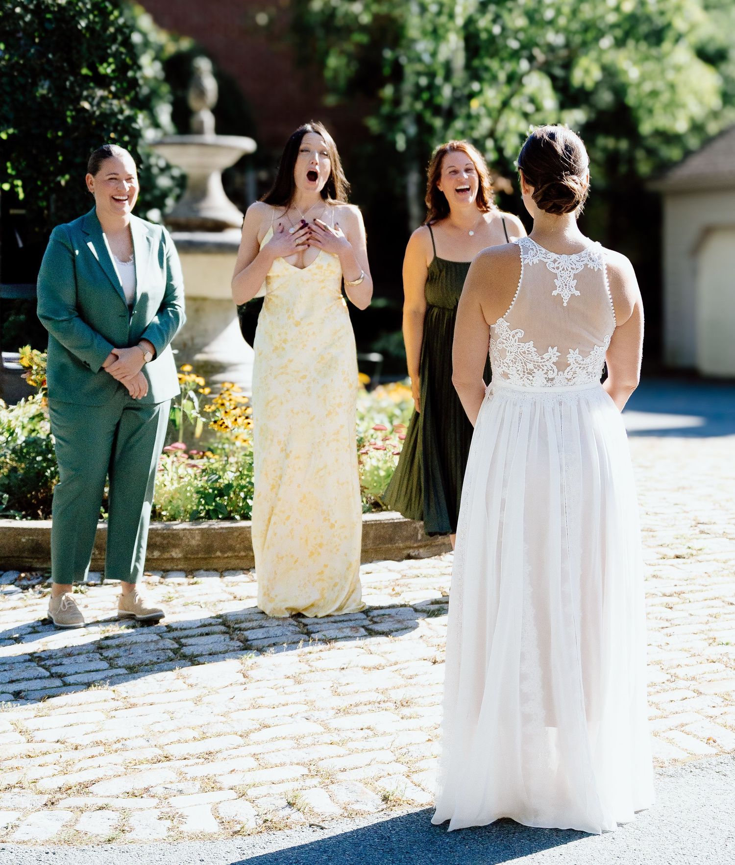 Wedding party in white dresses walking and laughing together on stone pathway.