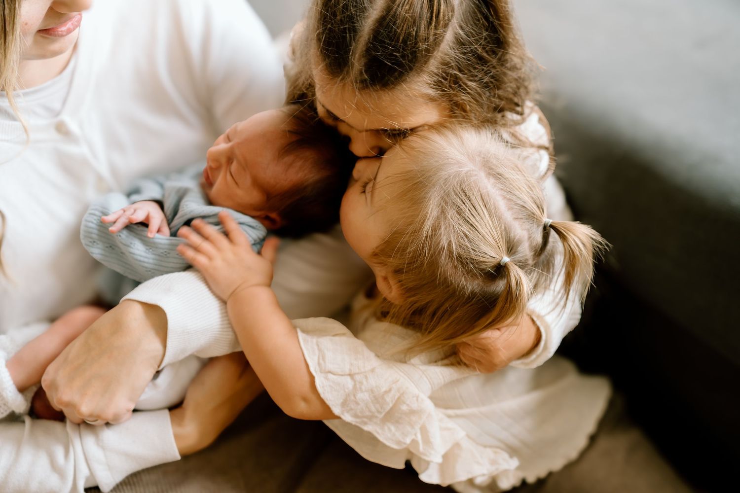 Family sharing tender moments together while relaxing on a cozy bed in white and neutral tones.
