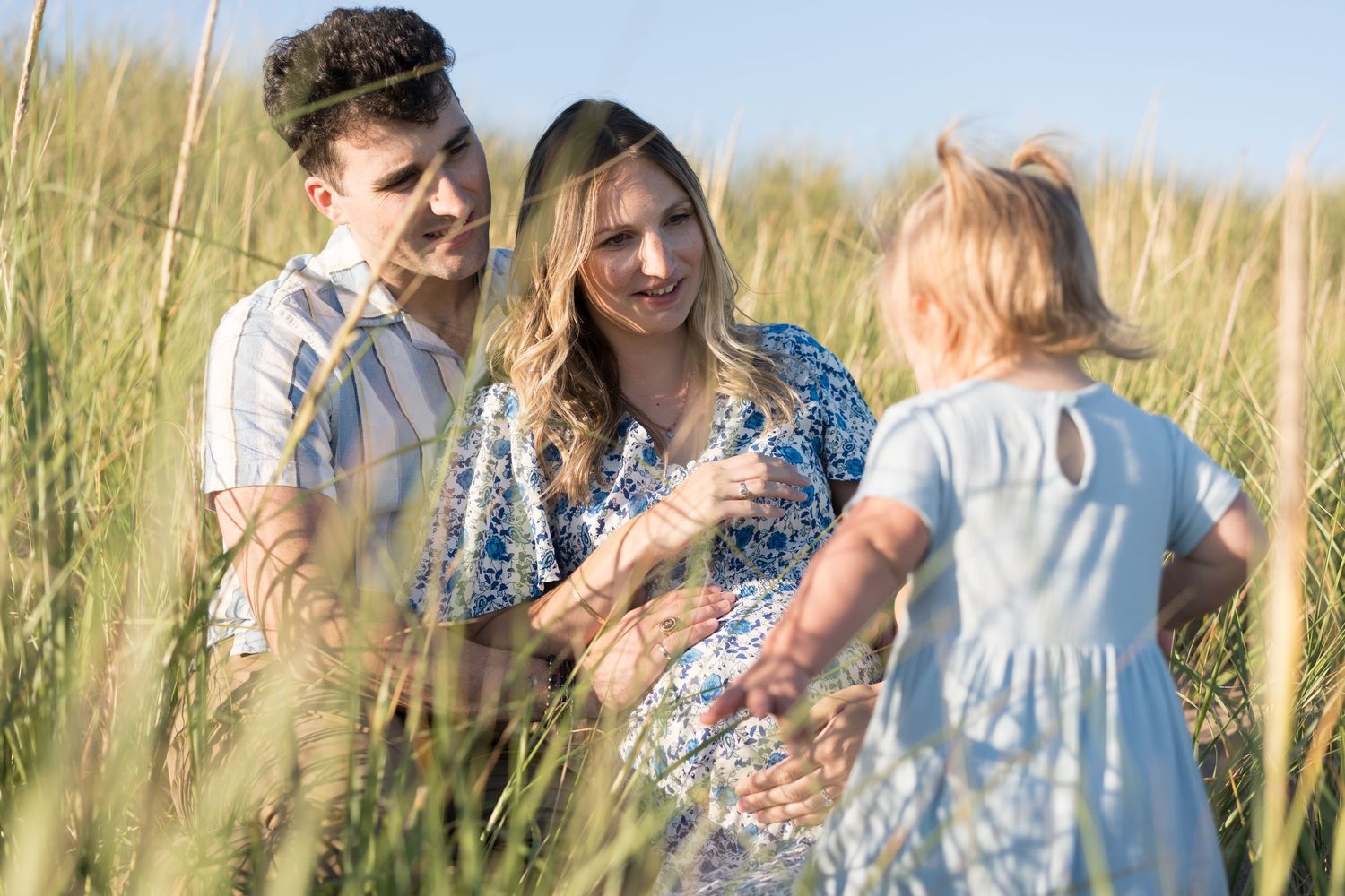 Candid family moments captured in a field of tall grass during sunset.