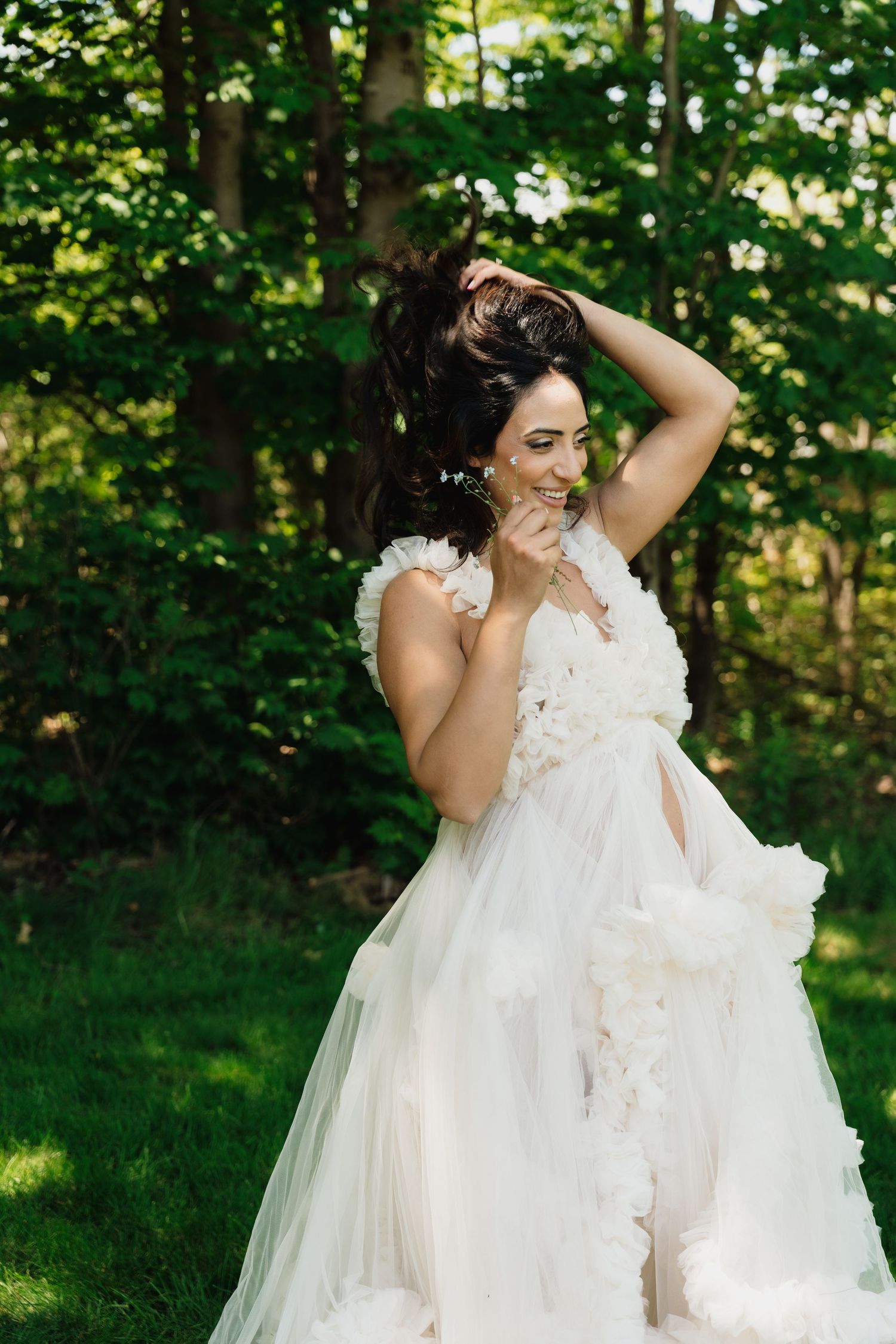 Smiling bride in a white floral tulle gown posing outdoors in a lush green garden setting.