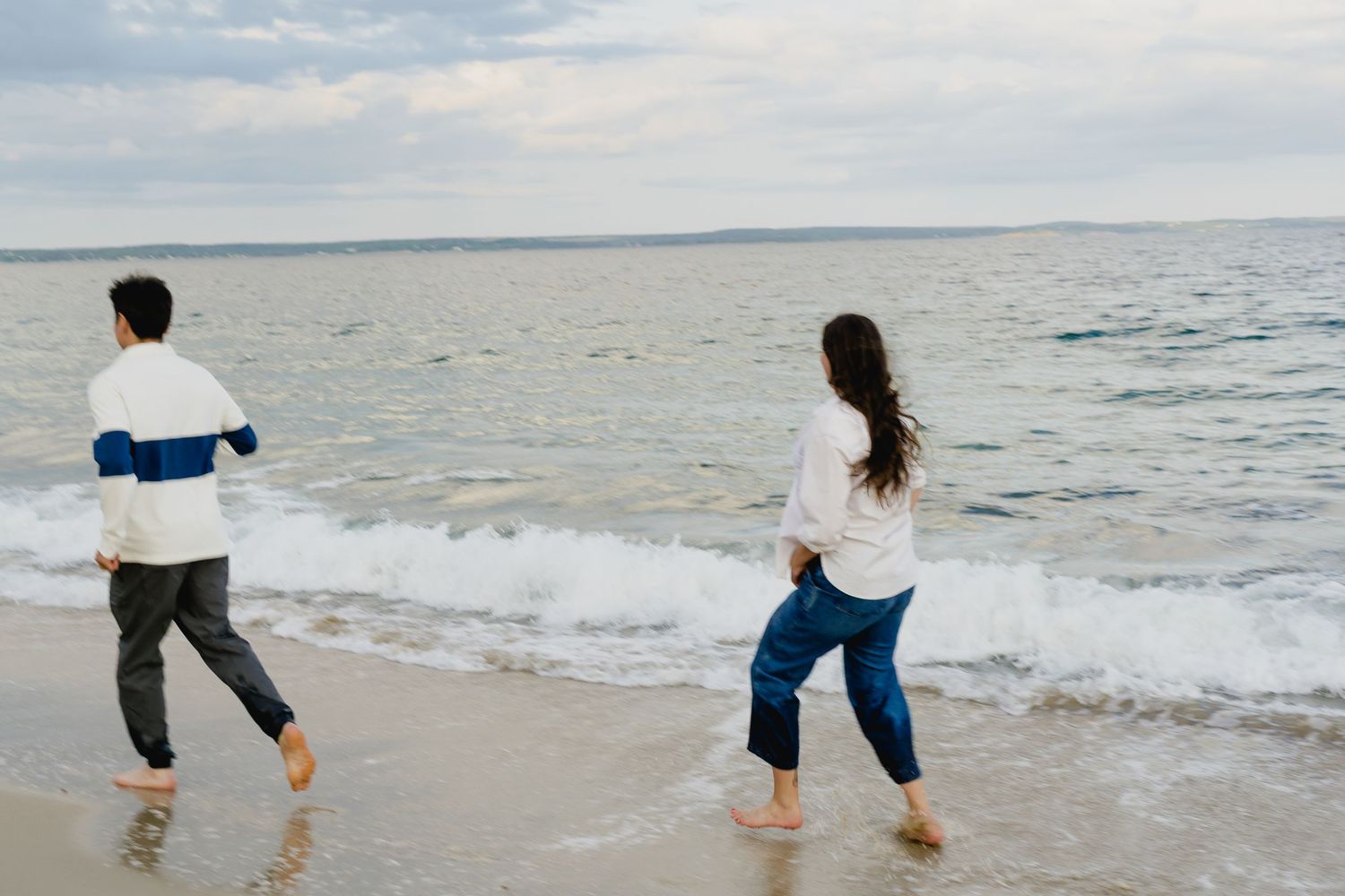 People strolling along beach shoreline in casual attire with waves rolling in.