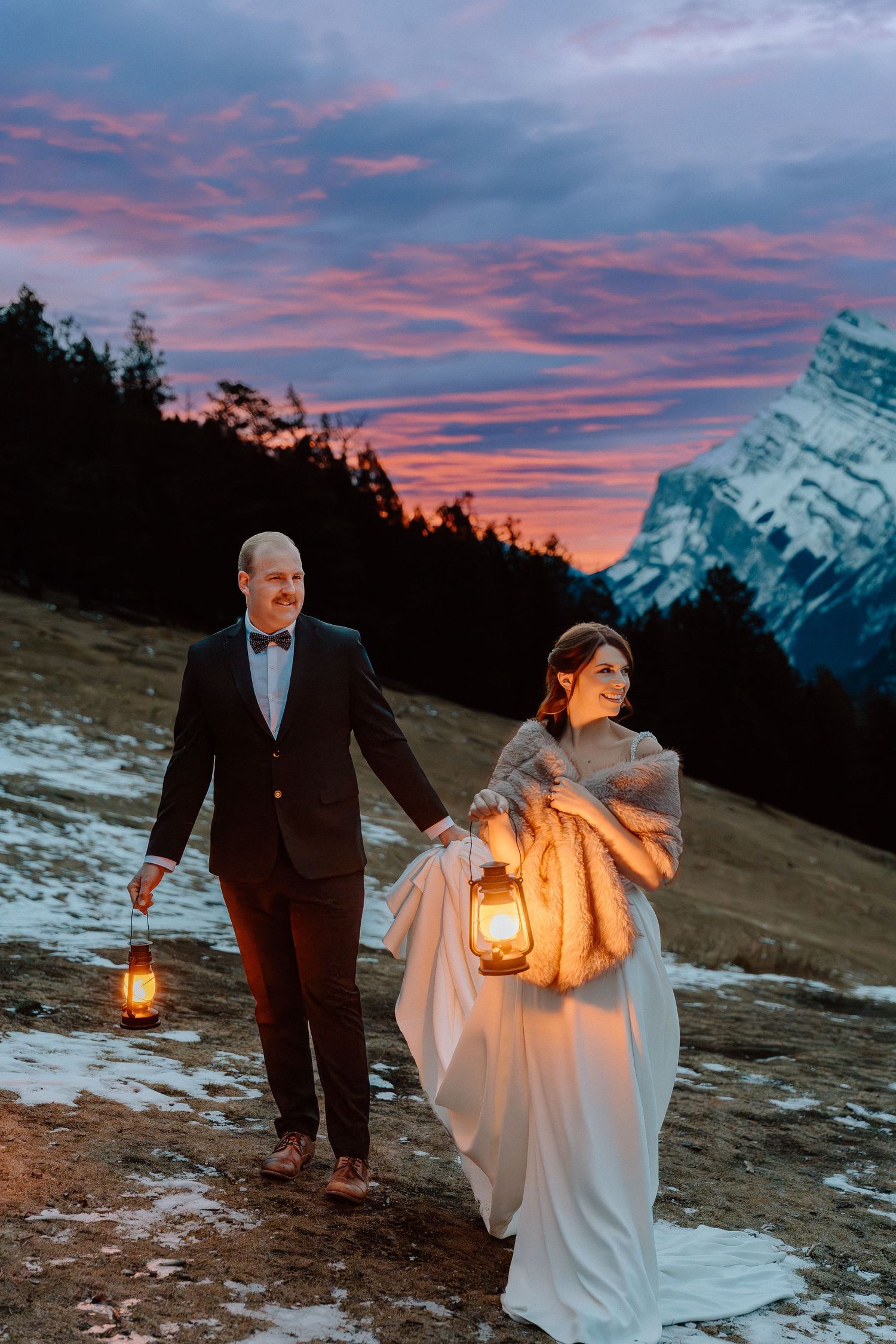 Couple with lanterns walking at dusk with mountain peaks and pink sky.