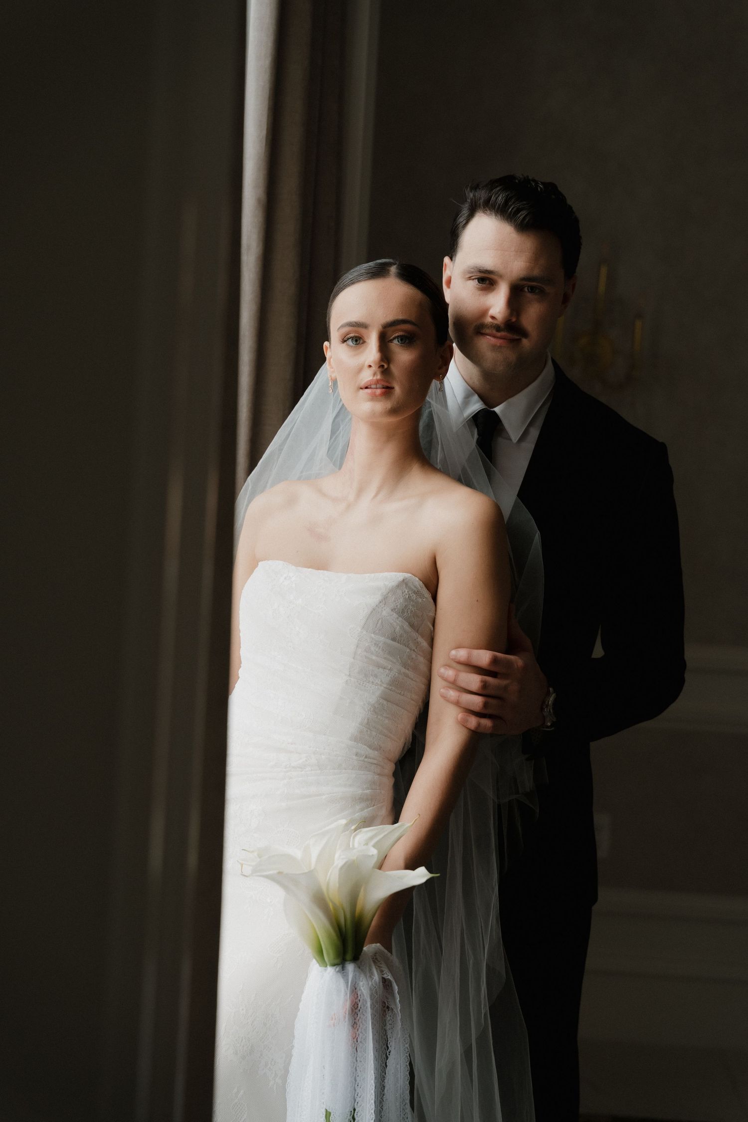 Romantic wedding portrait series showing couple in elegant embrace against moody dark background.