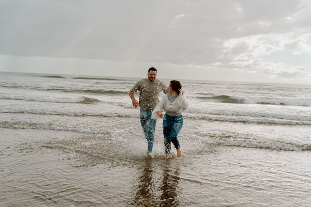 Couple splashing and playing in ocean waves wearing casual denim outfits.