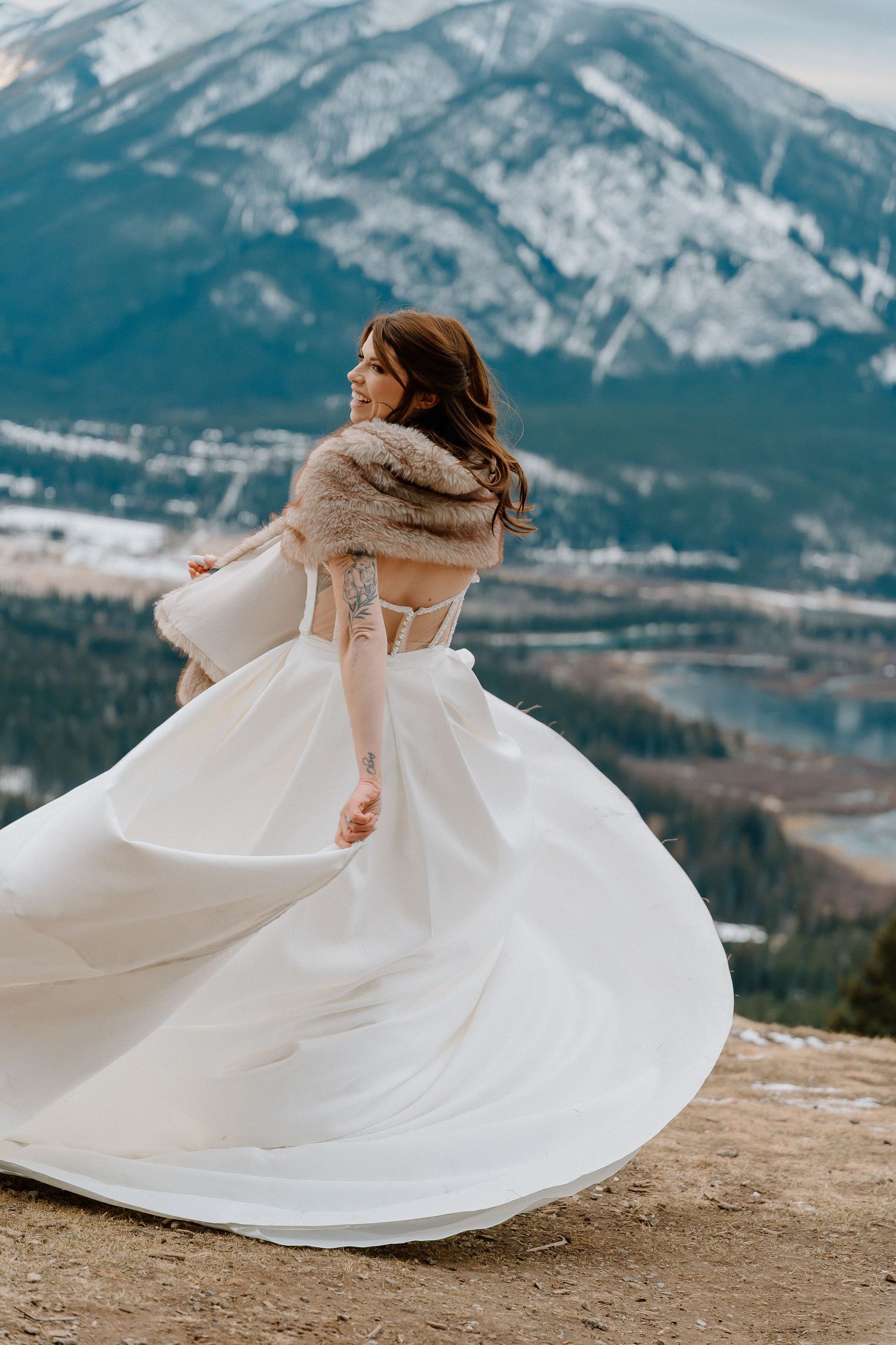 Bride twirling in white dress against mountain backdrop with snow.