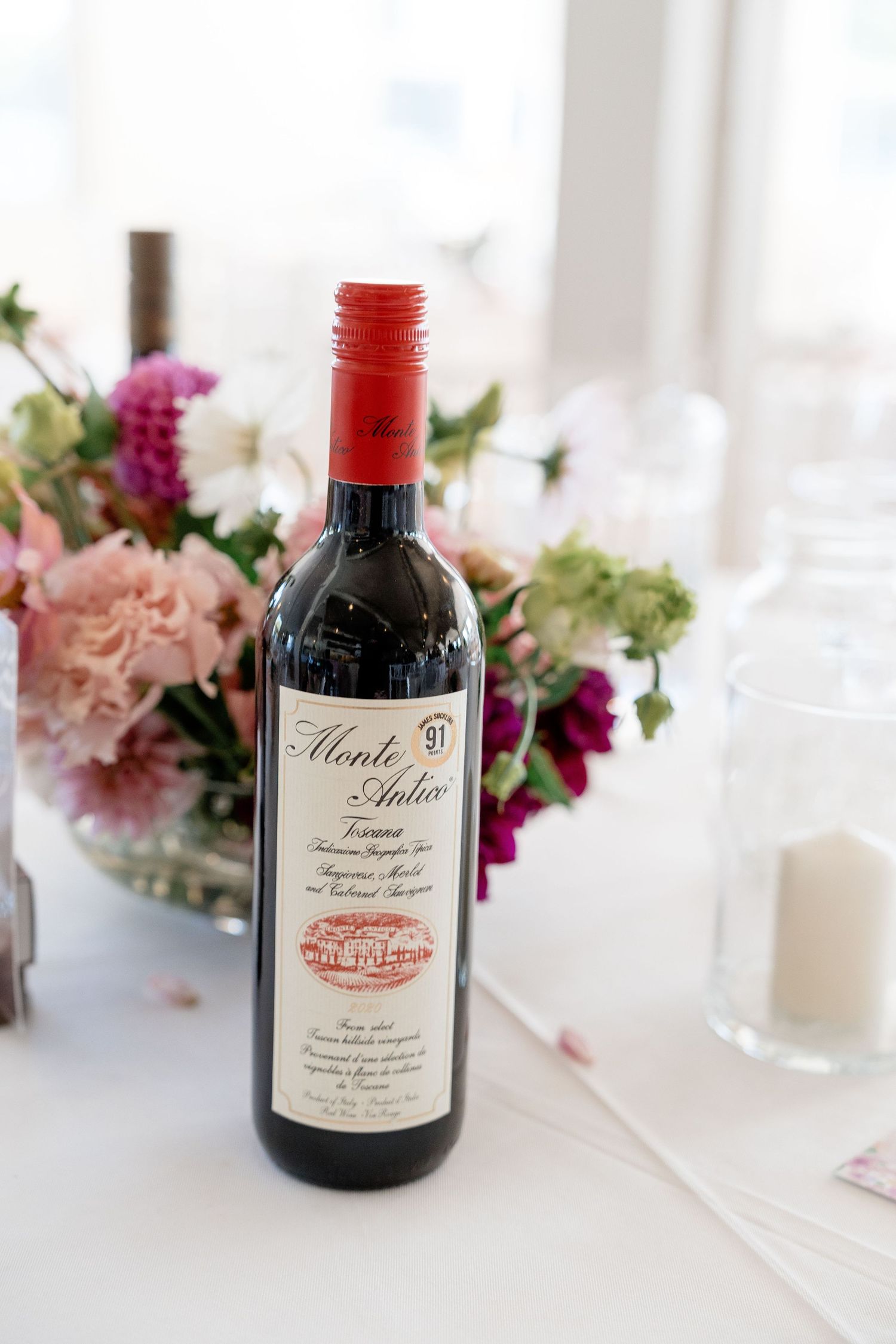 Wedding table decor featuring wine bottles and pink floral arrangements on white tablecloth.