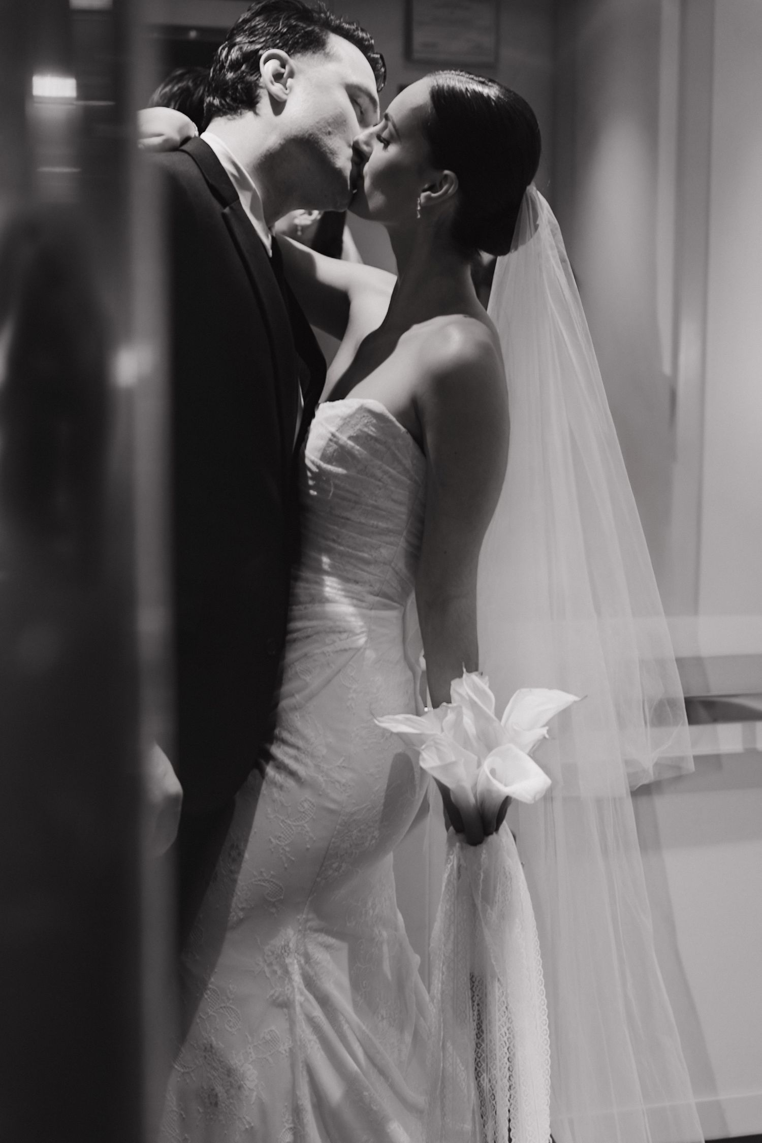 A romantic black and white wedding photograph showing a tender kiss between newlyweds, with the bride in a flowing gown and veil.